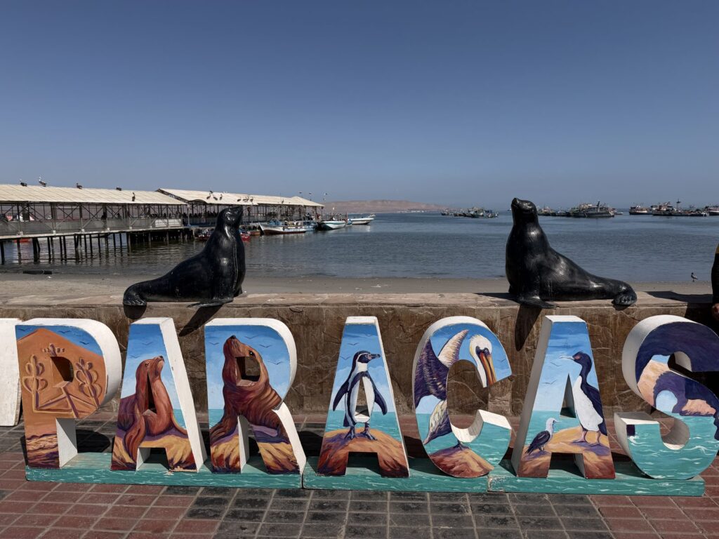 Letrero de Paracas con lobos marinos frente al muelle de la bahía